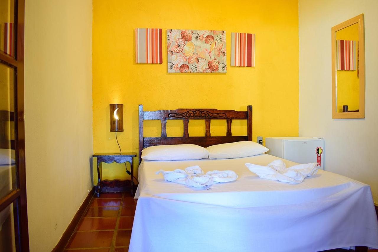 Quarto de casal com parede amarela, cabeceira de madeira e frigobar