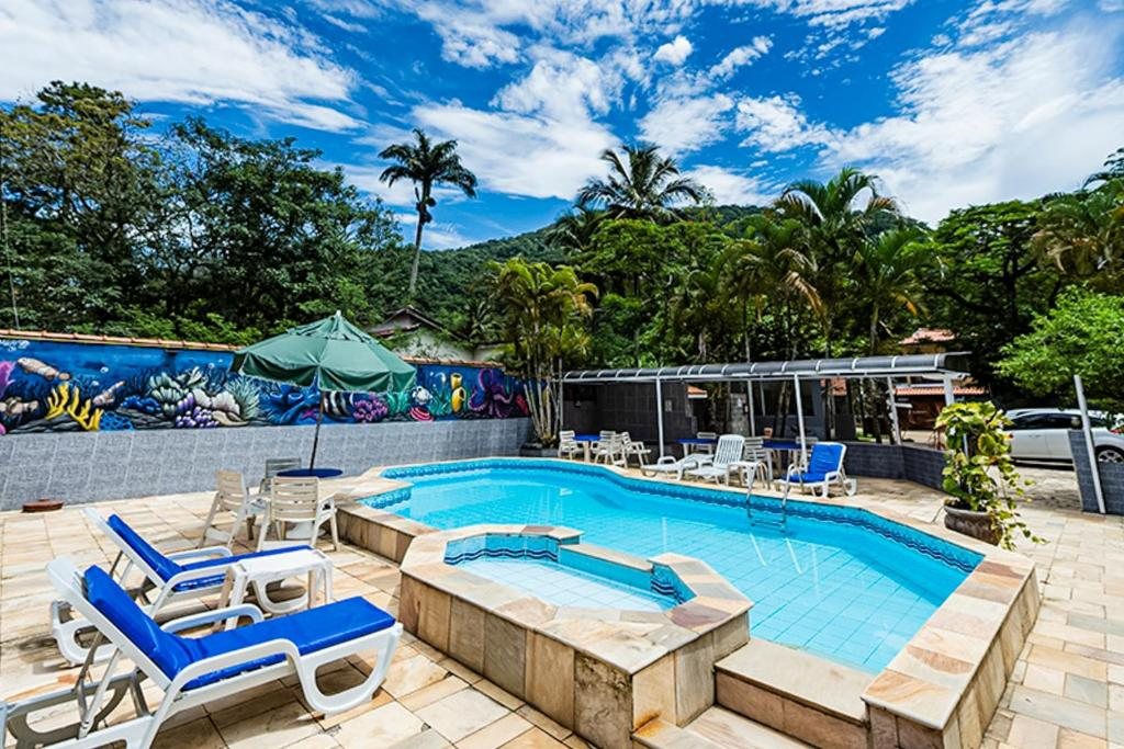 Piscina da Pousada Ubatuba Tropical com espreguiçadeiras, palmeiras e a serra ao fundo