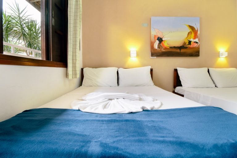 Quarto com duas camas de casal, arandelas e quadro colorido
